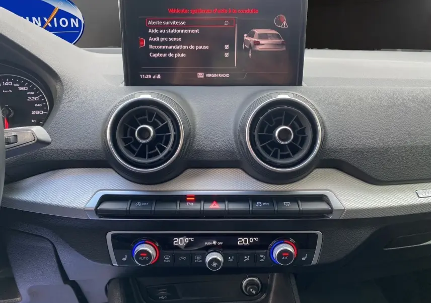Tableau de bord intérieur d'Audi Q2 2023 avec écran central affichant aides à la conduite et commandes climatisation.