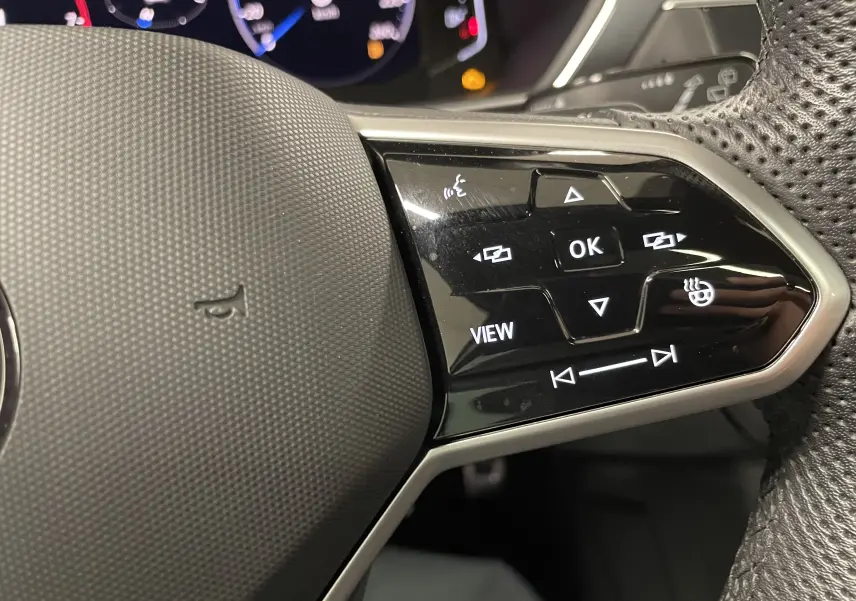Gros plan sur les commandes du volant à droite du Volkswagen Tiguan 2024, avec tableau de bord numérique en arrière-plan.