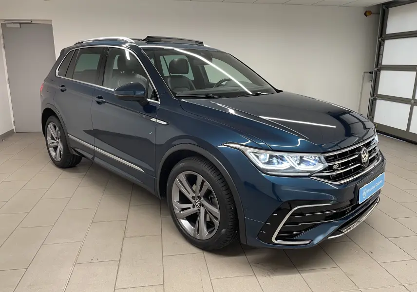 Volkswagen Tiguan 2024 bleu Nightshade en 3/4 avant droit, avec feux allumés et crochet d'attelage escamotable visible.