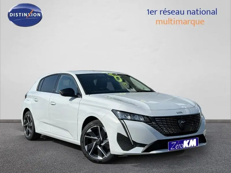 Vue 3/4 avant gauche d'une Peugeot 308 blanche avec jantes alliage et calandre noire distinctive.