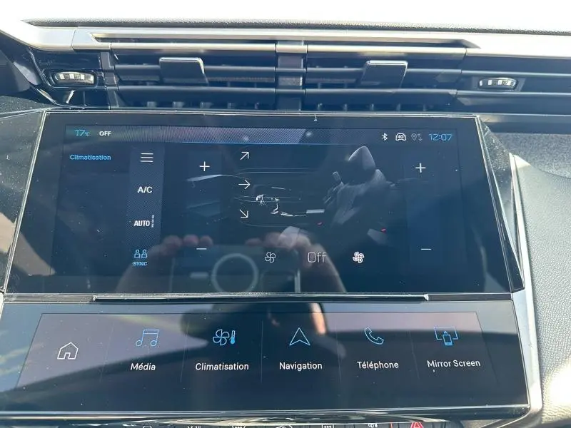 Écran tactile central de la Peugeot 308 bleu, vue rapprochée du système multimédia et climatisation.