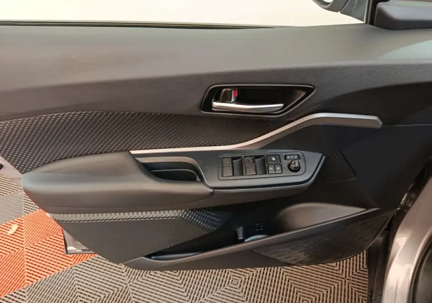 Vue rapprochée de la porte avant gauche du Toyota C-HR gris clair, avec commandes des vitres et poignée intérieure.