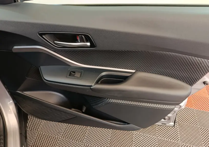 Gros plan sur la porte intérieure côté conducteur du Toyota C-HR gris clair, montrant la poignée et les commandes de fenêtre.