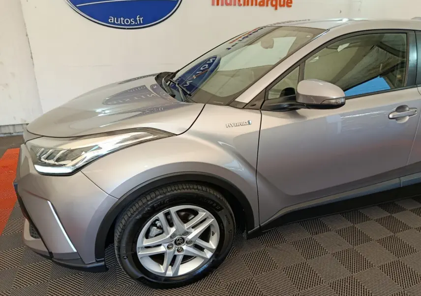 Vue 3/4 avant droit du Toyota C-HR gris clair hybride avec jante alliage et badge Hybrid visible sur l'aile.