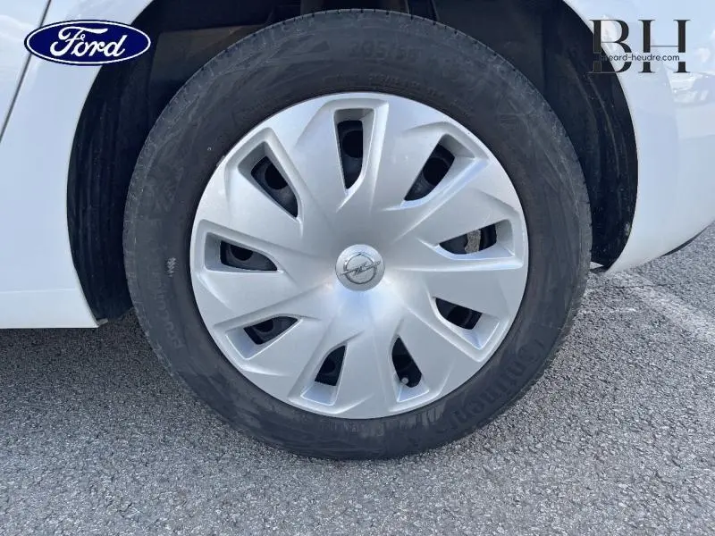 Gros plan sur la roue avant droite d'une Opel Astra blanc glacier avec enjoliveur argenté et logo Opel central.