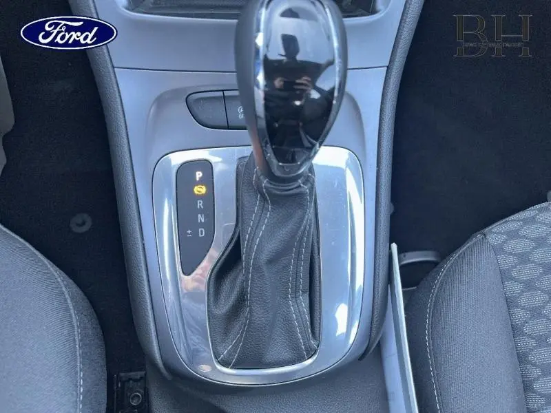 Gros plan sur la commande de boîte automatique noire et chrome de l’Opel Astra blanche, avec sellerie grise visible.