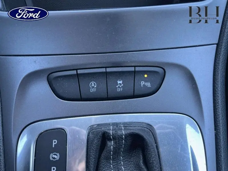 Gros plan sur les commandes de la console centrale d'une Opel Astra blanche, avec bouton de parking actif éclairé.