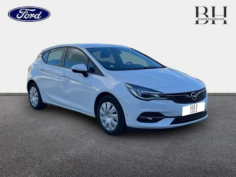 Opel Astra blanc glacier vue 3/4 avant droit, avec phares LED et enjoliveurs d'origine visibles.