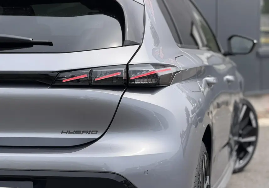 Vue 3/4 arrière droite d'une Peugeot 308 Hybrid gris Artense avec feux arrière LED à 3 griffes et jantes bi-tons.