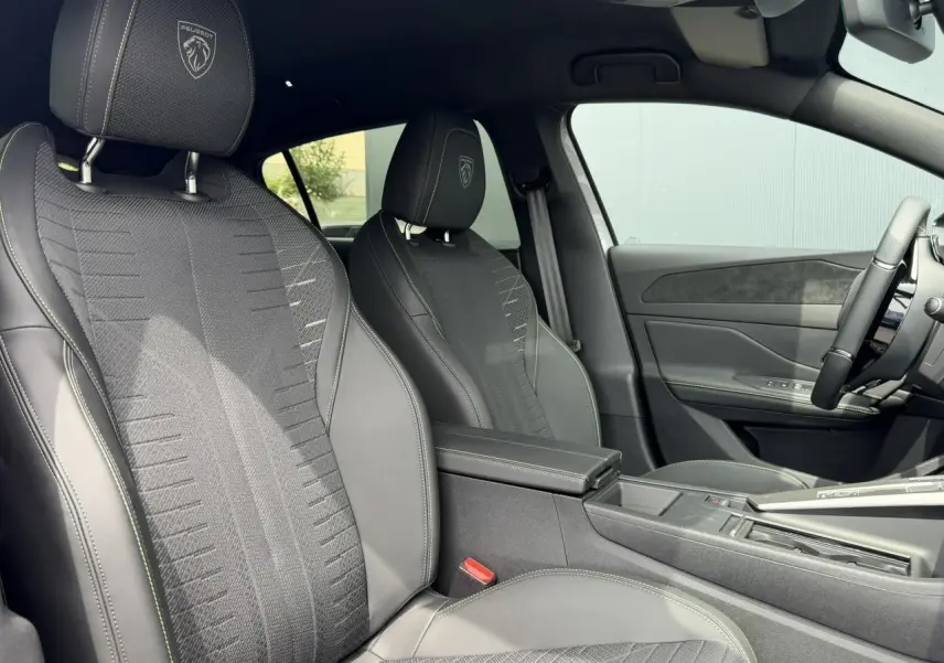Vue intérieure côté gauche des sièges avant noirs avec surpiqûres vert Adamite et blasons Peugeot embossés sur appuie-têtes.
