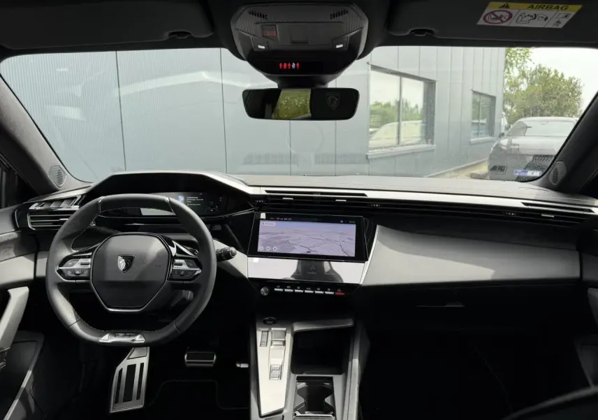 Vue avant de l'intérieur du Peugeot 308 gris Artense, avec volant compact GT et écran tactile central.
