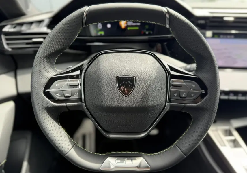 Volant compact en cuir noir avec surpiqûres vertes et logo GT au centre d'une Peugeot 308 NV Hybrid 2026.