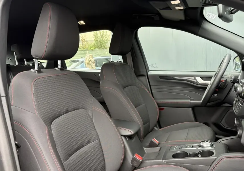 Vue intérieure côté conducteur du Ford Kuga 2023, sièges gris avec surpiqûres rouges et volant ST-Line à méplat.