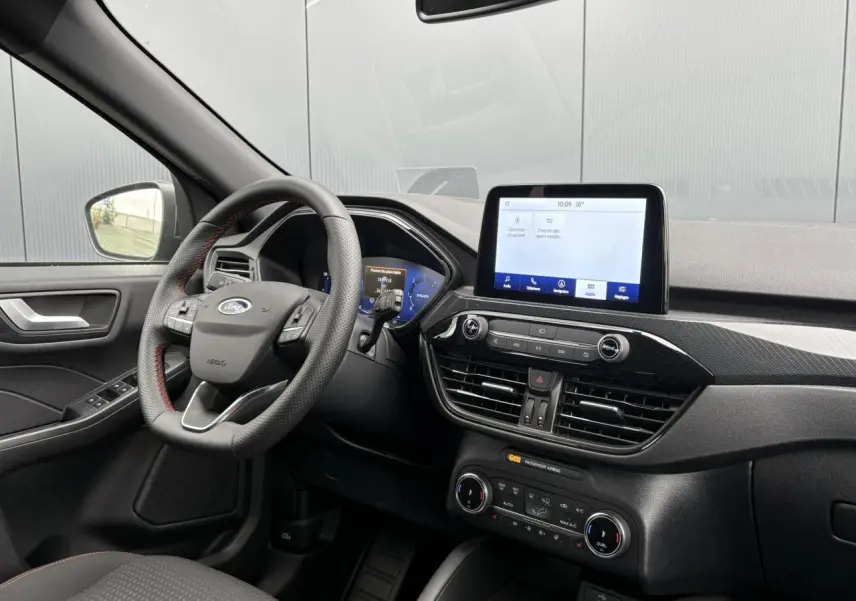 Vue intérieure côté conducteur du Ford Kuga gris graphite 2023, volant ST-Line à surpiqûres rouges et écran tactile central.