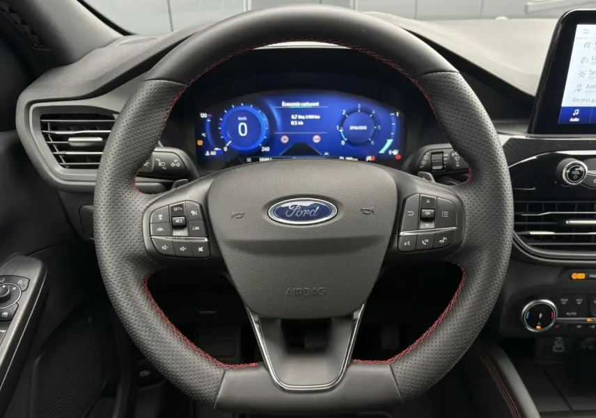 Vue rapprochée du volant perforé noir avec surpiqûres rouges du Ford Kuga 2023, tableau de bord numérique en arrière-plan.