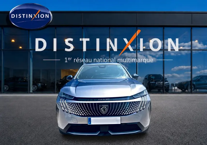 Vue frontale du Peugeot 5008 Hybrid 145 allure e-dcs6 gris artense devant une vitrine Distinxion.
