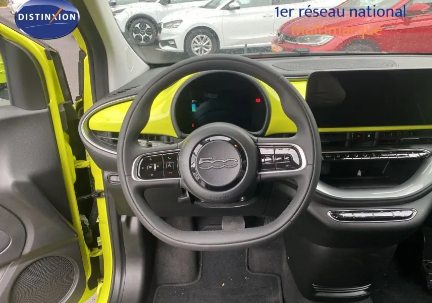 Vue intérieure avant de la Fiat 500 électrique 2024 jaune acid, avec volant multifonction et tableau de bord moderne.