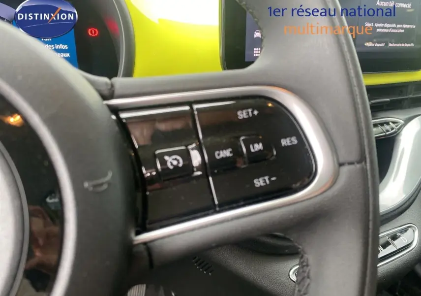 Gros plan sur le volant côté gauche d'une Fiat 500 électrique jaune acid, avec commandes de régulateur de vitesse visibles.