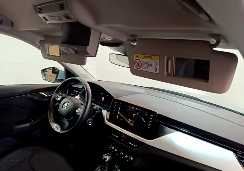 Intérieur du Skoda Kamiq 2022 vu côté conducteur, tableau de bord clair avec écran tactile et volant cuir multifonctions.