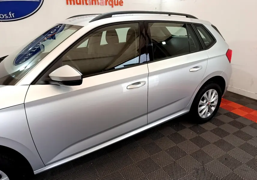 Profil côté gauche d'un Skoda Kamiq gris clair 2022 avec jantes alliage et rétroviseur blanc en intérieur showroom.