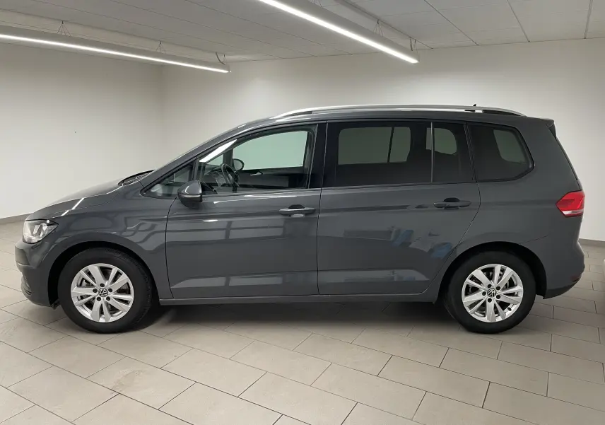 Profil droit d'un Volkswagen Touran 2024 gris dauphin, monospace diesel 7 places avec jantes alliage et toit équipé de barres longitudinales.