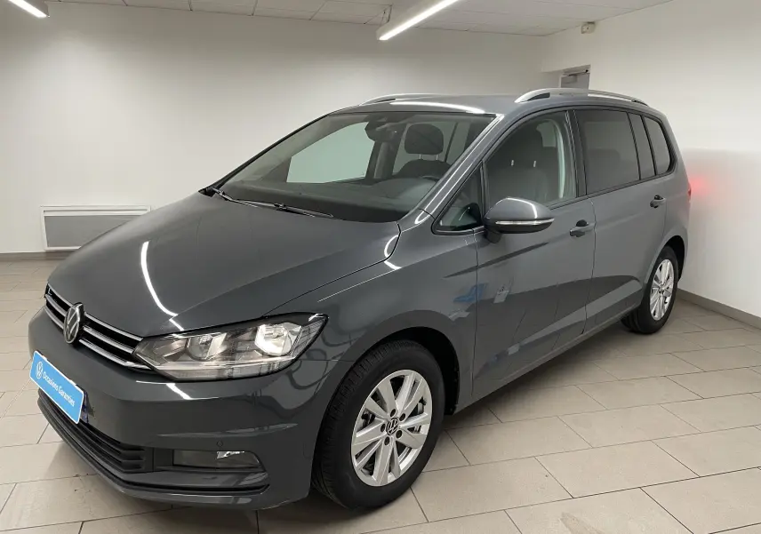 Volkswagen Touran gris dauphin en 3/4 avant droit, avec jantes alliage et toit équipé de barres de toit.