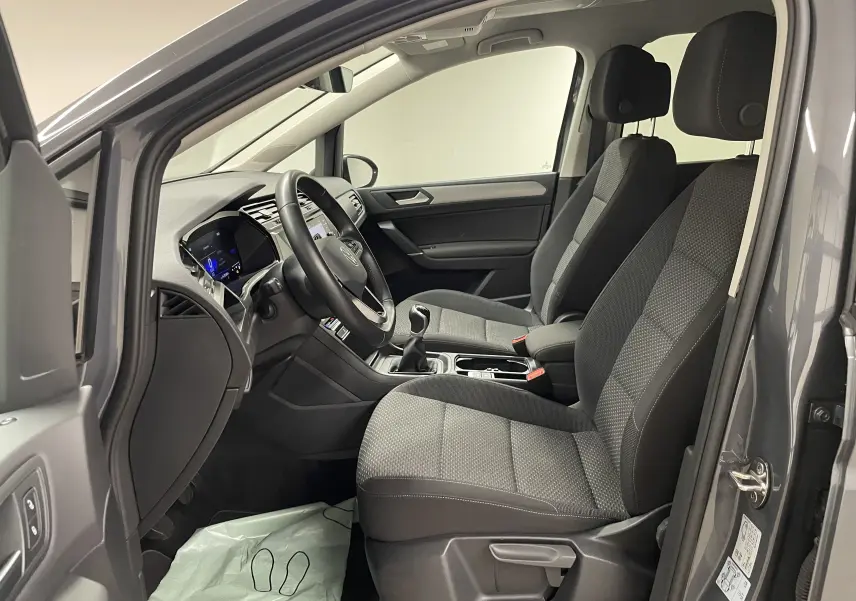Vue intérieure côté conducteur du Volkswagen Touran gris Dauphin 2024, sièges tissu et tableau de bord moderne avec boîte manuelle.