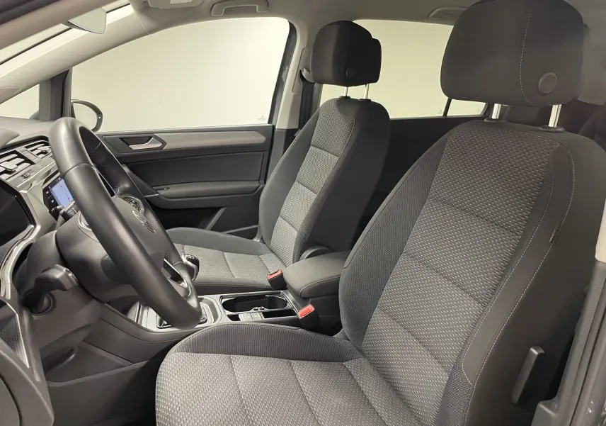 Vue intérieure côté conducteur du Volkswagen Touran 2024, sièges tissu gris et console centrale avec boîte manuelle.