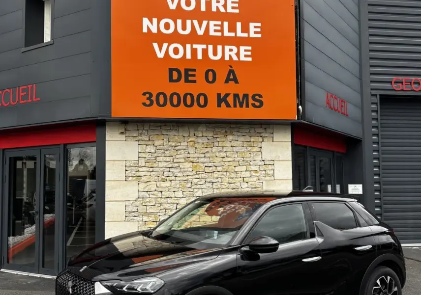 DS3 noir vue 3/4 avant droit, avec calandre distinctive et jantes noires, devant un bâtiment commercial.