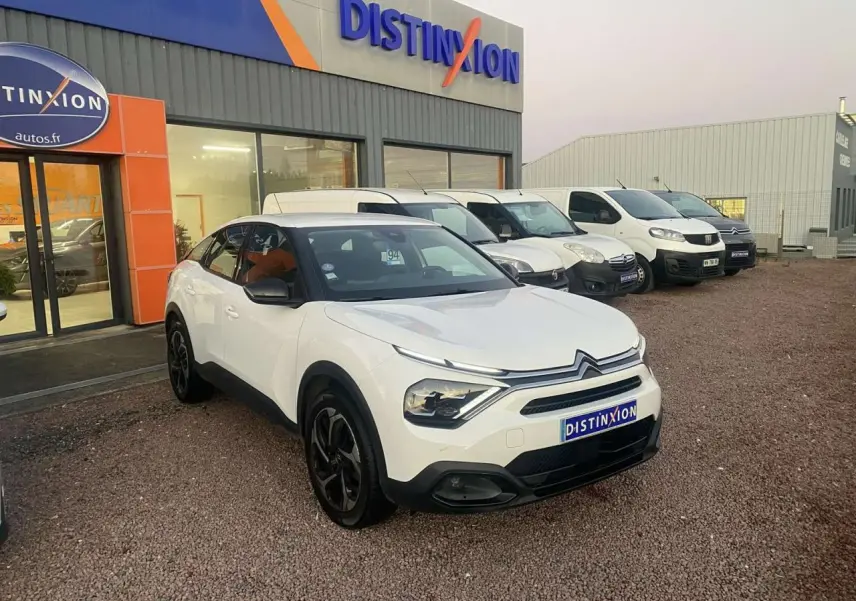 Citroën C4 blanc vue 3/4 avant droit, avec calandre distinctive et jantes noires, devant un garage Distinxion.