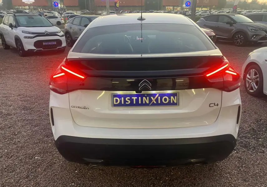 Vue arrière d'une Citroën C4 blanche 2021 avec feux arrière allumés et plaque Distinxion visible.