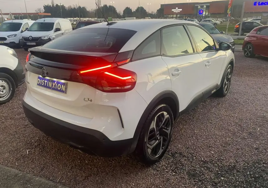 Vue 3/4 arrière droite d'une Citroën C4 blanche 2021 avec feux arrière allumés et toit noir contrastant.
