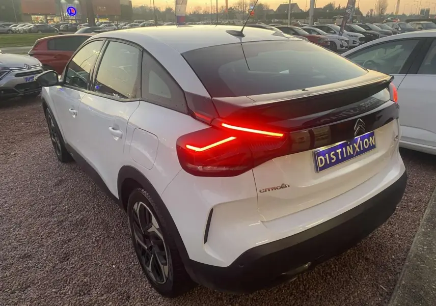 Vue 3/4 arrière droite d'une Citroën C4 blanche de 2021 avec feux arrière allumés et toit noir contrastant.
