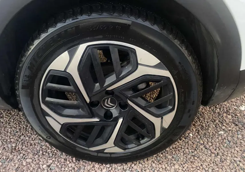 Gros plan sur la roue avant droite d'une Citroën C4 blanche avec jante alliage noire et argentée au design géométrique.