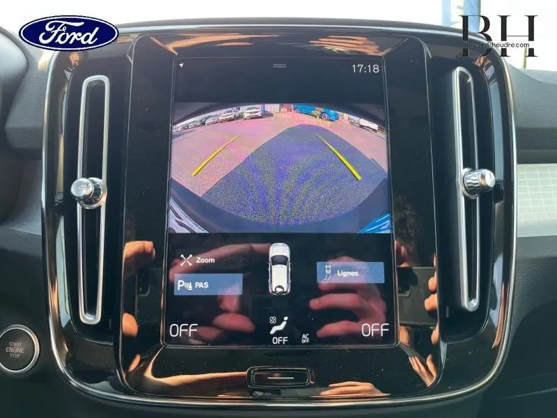 Écran central du tableau de bord montrant la caméra de recul d'un Volvo XC40 gris Glacier, interface tactile avec options visibles.