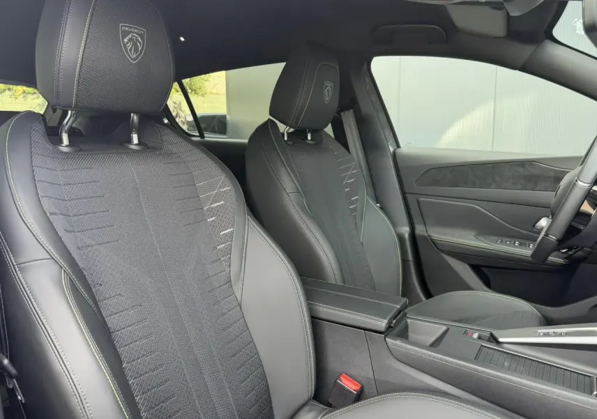 Vue intérieure côté droit des sièges avant noirs avec surpiqûres vert Adamite et logo Peugeot embossé sur appuie-têtes.