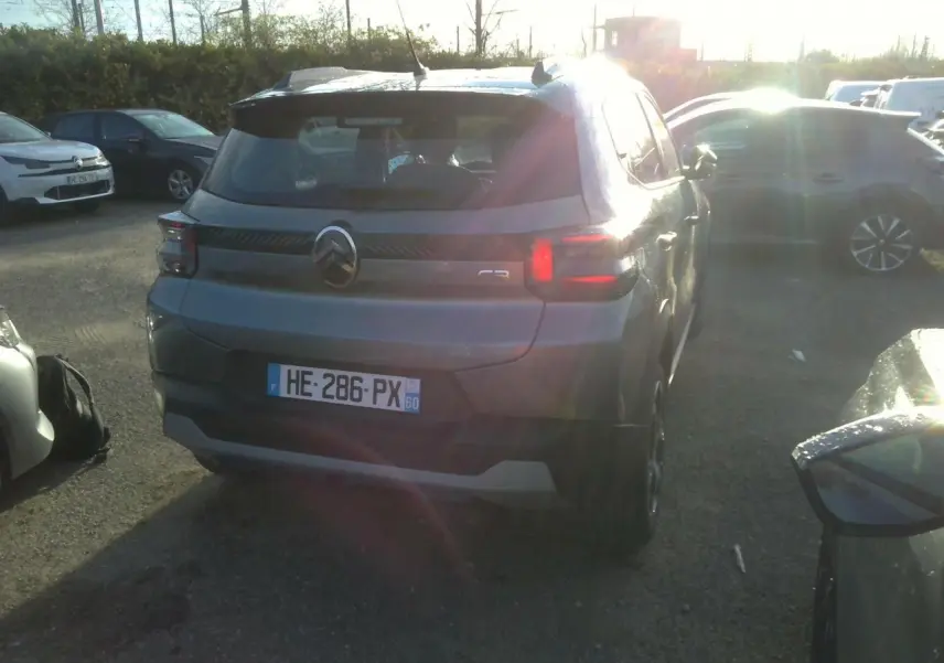Vue 3/4 arrière d'une Citroën C3 gris foncé avec barres de toit noir brillant et feux arrière LED allumés.