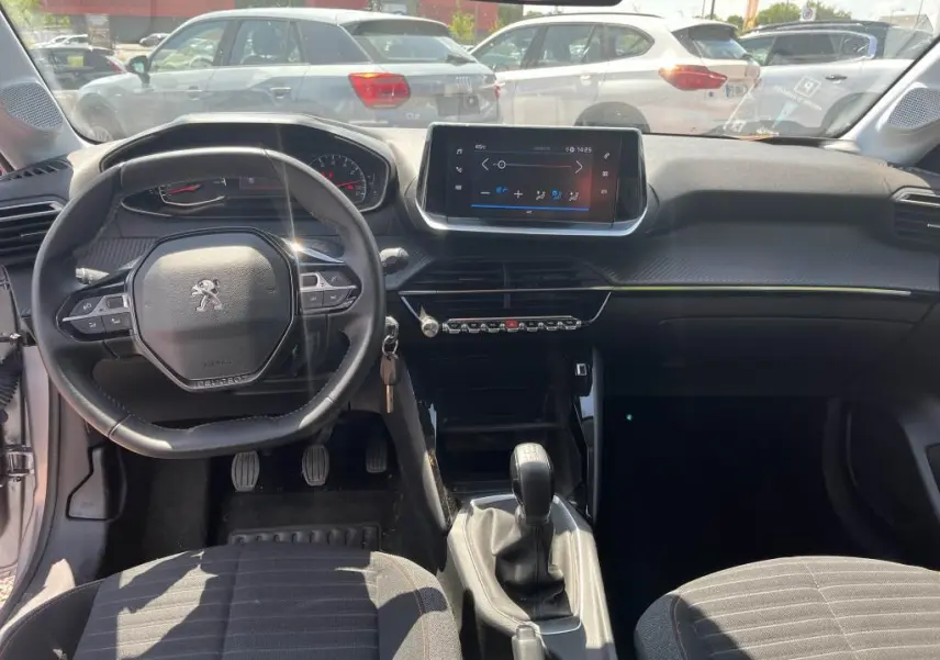 Vue intérieure avant de la Peugeot 208 gris clair 2023, avec volant compact, écran tactile et boîte manuelle visible.