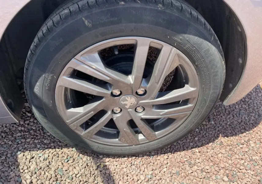 Gros plan sur la roue avant droite d'une Peugeot 208 gris clair 2023 avec jante alliage et logo lion au centre.