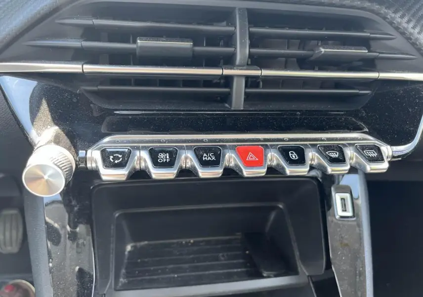 Vue rapprochée des commandes centrales chromées et boutons fonctionnels sur tableau de bord noir brillant d’une Peugeot 208 gris clair 2023.