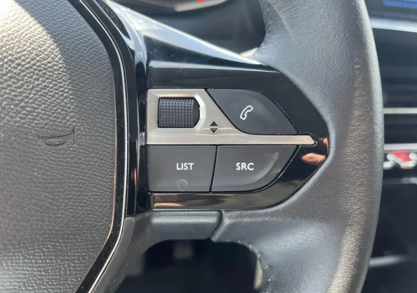 Gros plan sur les commandes gauche du volant noir du Peugeot 208 gris clair 2023, avec boutons LIST, SRC et téléphone.