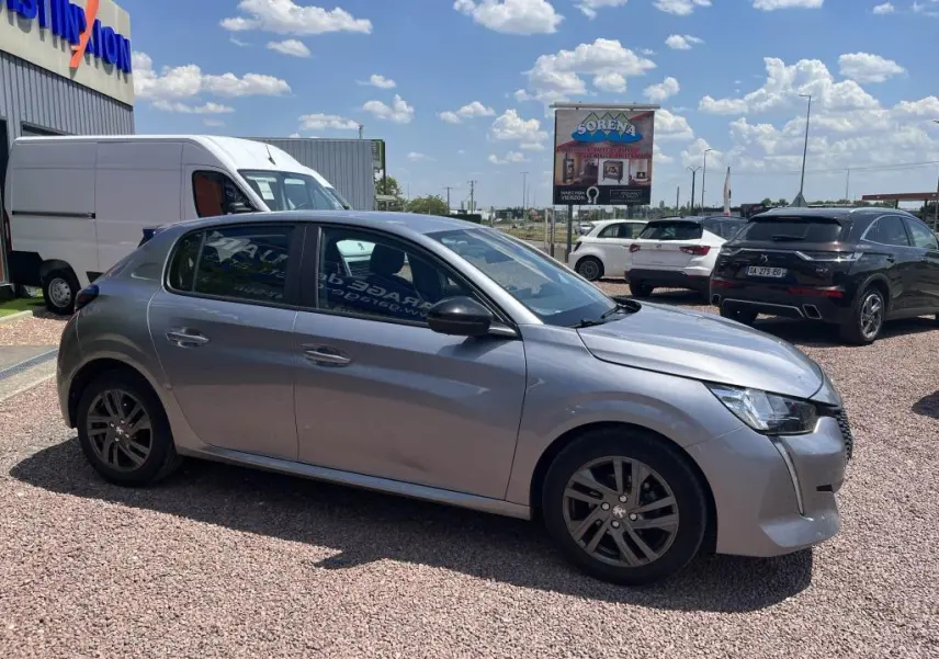 Peugeot 208 gris clair vue de profil côté gauche sur parking extérieur avec jantes alliage et calandre distinctive.
