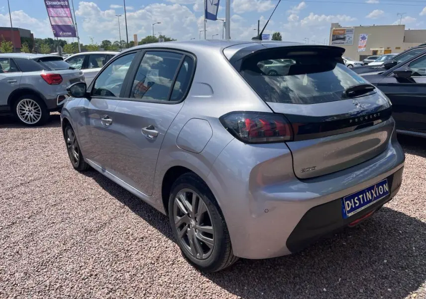 Peugeot 208 gris clair vue 3/4 arrière droit, avec feux arrière noirs et toit légèrement surélevé, en extérieur sur parking.
