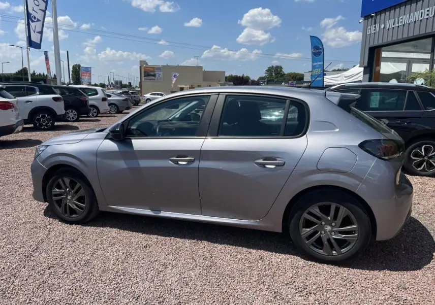 Peugeot 208 gris clair vue de profil côté gauche, avec jantes alliage et toit légèrement incliné vers l'arrière.