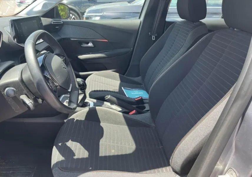 Vue intérieure côté conducteur de la Peugeot 208 1.2i PureTech 75 Active Pack 2023 avec sièges tissu noirs et volant compact.