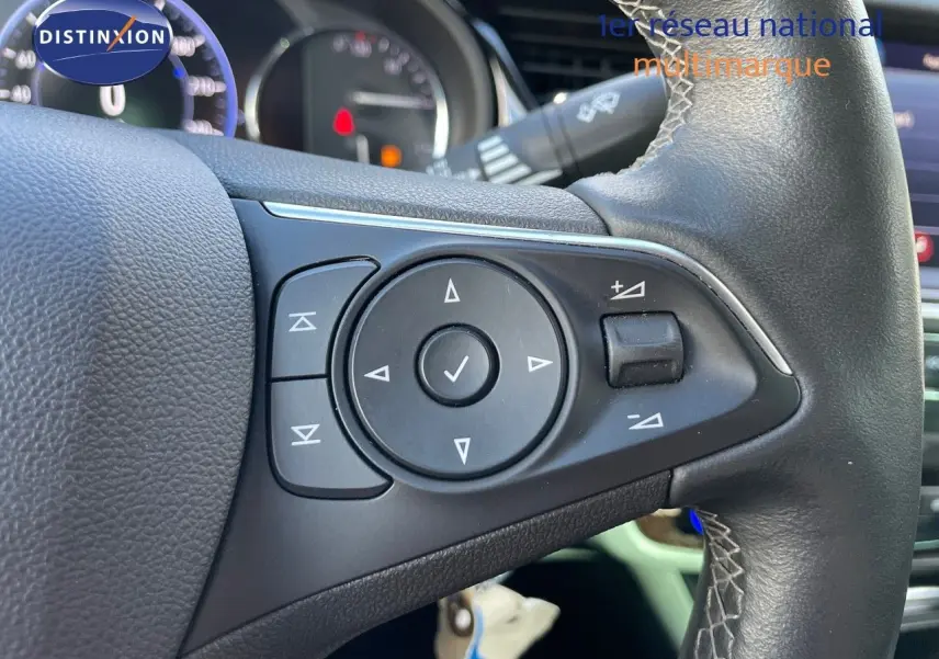 Gros plan sur les commandes au volant en cuir noir de l'Opel Insignia gris minéral métal, tableau de bord en arrière-plan.