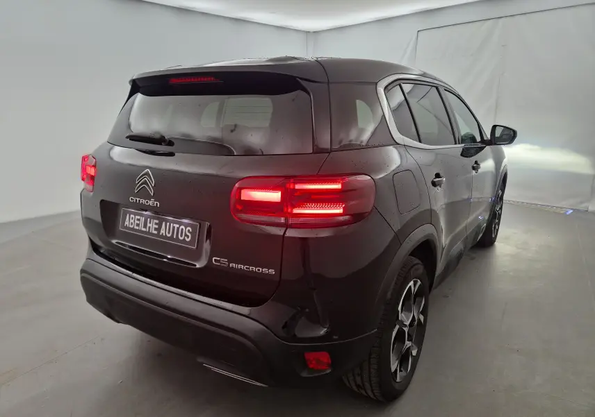 Vue 3/4 arrière droite d'un Citroën C5 Aircross noir 2024 avec feux arrière allumés dans un studio lumineux.