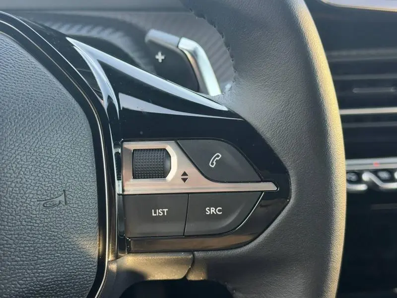 Gros plan sur les commandes gauche du volant noir du Peugeot 2008 rouge Elixir, avec molette et boutons d’appel.