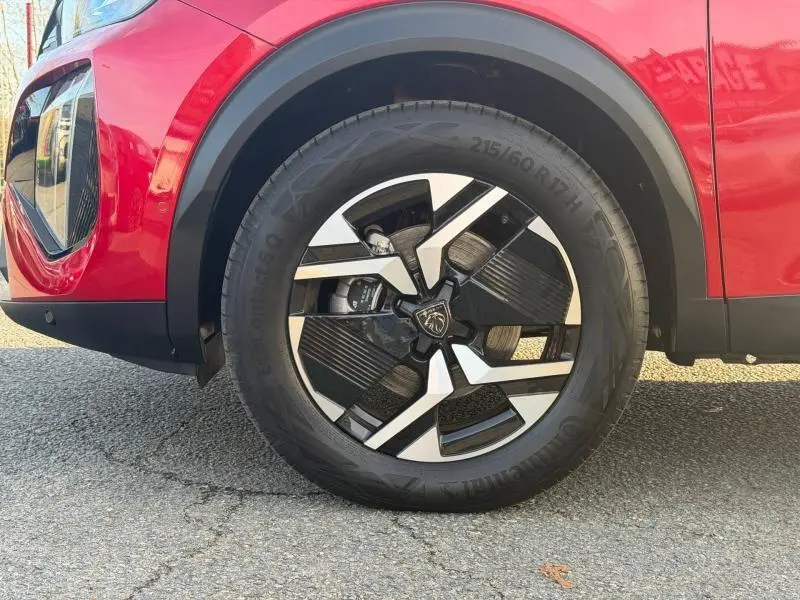 Gros plan sur la roue avant gauche du Peugeot 2008 rouge Elixir avec jante alu noire et argentée au design moderne.