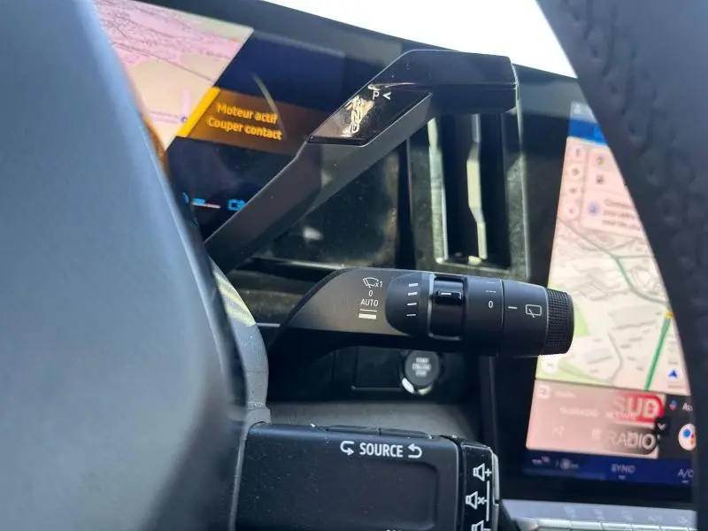 Gros plan sur la commande d’essuie-glace à gauche du volant du Renault Austral Bleu Iron, avec écran tactile et affichage digital en arrière-plan.